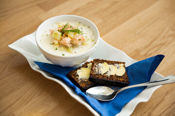 A bowl of Finnish Lohikeitto soup served on wooden table with a piece of Swedish rye bread. Creamy broth, tender potatoes, and flaky pink salmon create a delicious dish. 