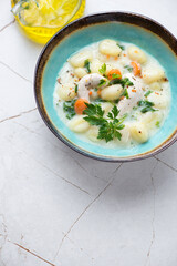 Turquoise bowl with chicken gnocchi soup on a white granite background, vertical shot with space, elevated view