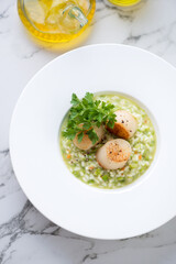 Pea risotto with pan seared scallops served in a white plate, above view on a light-grey marble background, vertical shot