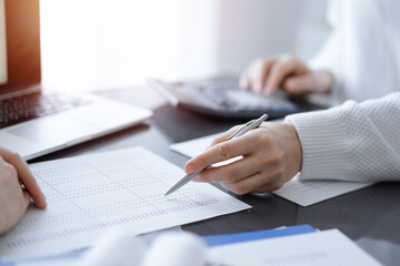 Woman accountant using a calculator and laptop computer while counting taxes for a client. Business...