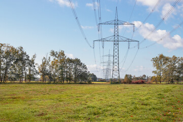 High-voltage transmission line in a field among trees against a blue cloudy sky