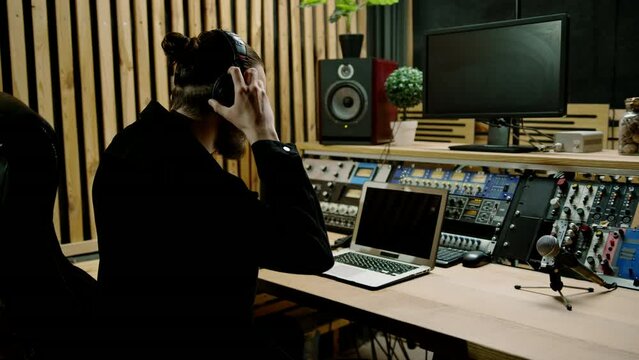 young sound engineer putting on headphones working in a professional music studio with monitors and an equalizer mixing and mastering tracks