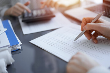 Woman accountant using a calculator and laptop computer while counting taxes for a client. Business...
