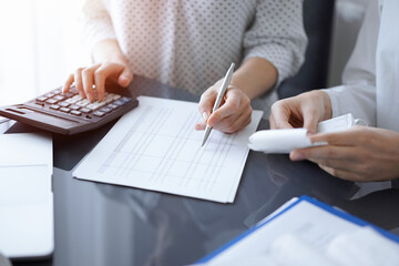Woman accountant using a calculator and laptop computer while counting taxes with a client or...