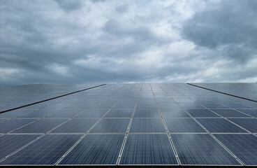 Solar panels of a photovoltaic plant on a roof, cloudy sky and cloud reflection on the panels