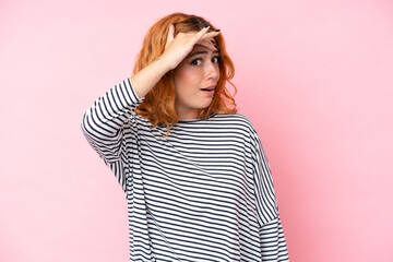 Young caucasian woman isolated on pink background doing surprise gesture while looking to the side