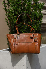close-up photo of brown leather bag on a flowerpot made of cement. outdoors photo