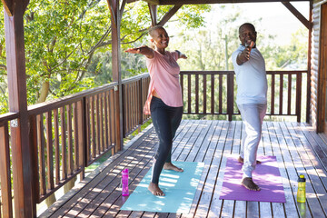 Happy senior african american couple practicing yoga on mats on terrace