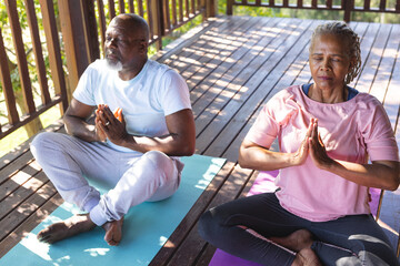Focused senior african american couple practicing yoga on mats on terrace