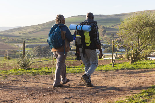 Senior african american couple with backpacks walking in sunny nature
