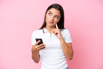 Young caucasian woman isolated on pink background using mobile phone and thinking