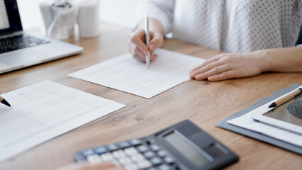 Woman accountant using a calculator and laptop computer while counting taxes with colleague at wooden desk in office. Teamwork in business audit and finance