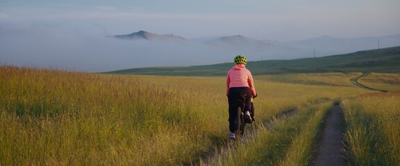 The woman is ride on bike against the backdrop of hills in dense fog at sunset in the picturesque...