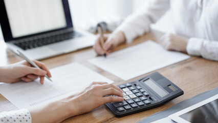 Two accountants using a laptop computer and calculator while counting taxes at wooden desk in office. Teamwork in business audit and finance