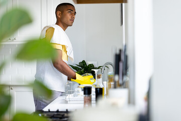Thoughtful biracial man washing up in kitchen sink, copy space