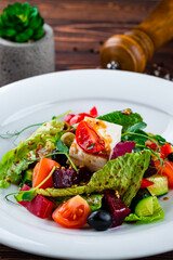 Salad of fresh cucumber, tomato, sweet pepper, lettuce, feta cheese, olives, beets and Dijon mustard in a plate.
