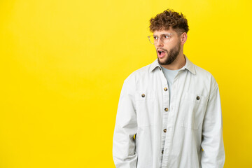 Young handsome caucasian man isolated on yellow background doing surprise gesture while looking to the side