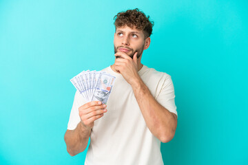 Young caucasian man taking a lot of money isolated on blue background and looking up