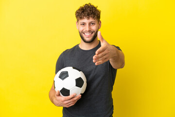 Handsome young football player man isolated on yellow background shaking hands for closing a good deal