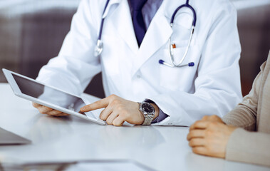 Unknown male doctor and patient woman discussing something while sitting in clinic and using tablet computer. Best medical service in hospital, medicine, pandemic stop