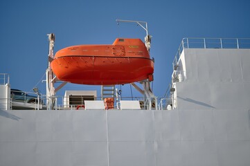 an orange lifeboat aboard a large passenger ferry ready to be launched and assisted at sea.