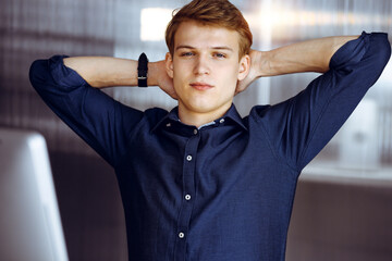 Young blond businessman and programmer stretching hands after working hard with computer in a...