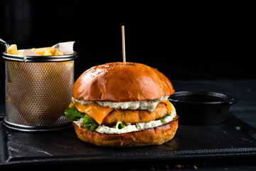 Chicken burger with cheddar cheese, lettuce, sauce, French fries and ketchup on a dark background,...