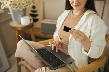 Young woman shopping online, using laptop and credit card, sitting in a cozy living room.