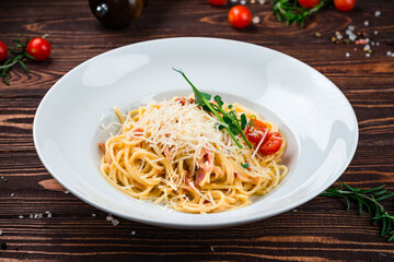 Spaghetti with bacon, cherry tomatoes, parmesan cheese and herbs in a plate.