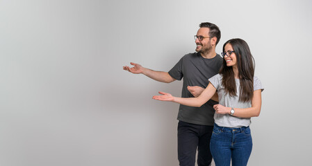 Smiling young boyfriend and girlfriend showing copy space for advertisement. Happy couple wearing eyeglasses and casuals presenting empty space for marketing against background