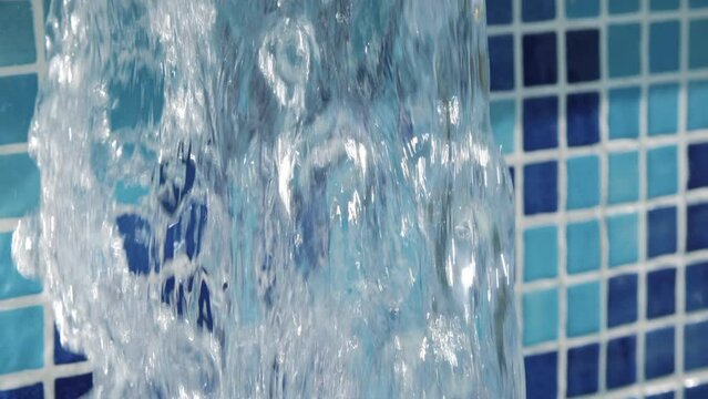 Large and dense jet of Water filling a Swimming Pool. Blue tiles on background. Extreme Close Up