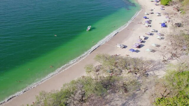 Popular Sandy Beach Shore With Tents And Boat On Ocean, Playa Conchal Costa Rica, 4K Drone