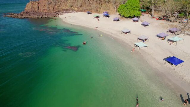 Popular Busy Beach Shore With Tourists Relaxing In Shade And Swimming, Conchal Beach Costa Rica 4K Drone