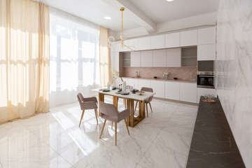 stylish kitchen and a set dining table in a light luxury interior design of a modern apartment in a minimalist style with marble trim and huge windows. daylight inside.