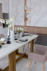 stylish kitchen and a set dining table in a light luxury interior design of a modern apartment in a minimalist style with marble trim and huge windows. daylight inside.