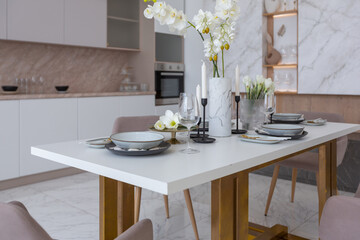 stylish kitchen and a set dining table in a light luxury interior design of a modern apartment in a minimalist style with marble trim and huge windows. daylight inside.