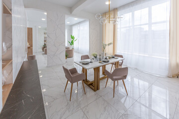Fototapeta na wymiar stylish kitchen and a set dining table in a light luxury interior design of a modern apartment in a minimalist style with marble trim and huge windows. daylight inside.