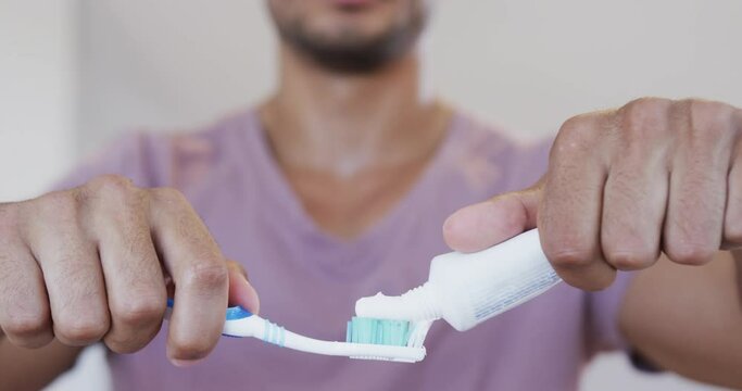 Close up of biracial man of biracial man applying toothpaste to toothbrush in bathroom, slow motion