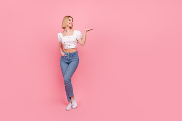 Fototapeta na wymiar Full size photo of pretty young lady promoter hold open palm beauty product wear shirt jeans shoes isolated pink color background