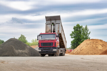 Dump truck with a raised body at a construction site. Transportation and unloading of sand or soil....
