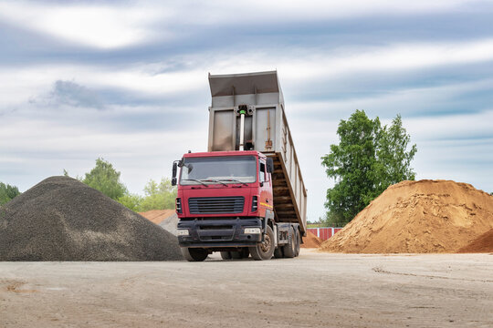 Dump Truck With A Raised Body At A Construction Site. Transportation And Unloading Of Sand Or Soil. Technique For Transportation Of Bulk Materials. Transportation Of Bulk Building Materials.