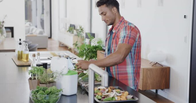 Biracial man preparing meal, composting vegetable waste in modern kitchen, slow motion