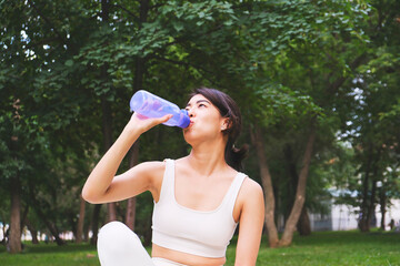 Asian sportif girl is drinking water from bottle in park outdoor.