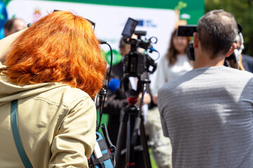 Red hair female camerawoman filming media event or press conference with a video or television...
