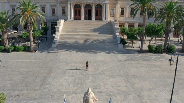 Drone shot of a woman walking towards the city hall of Ermoupoli in Syros, Greece during sunrise