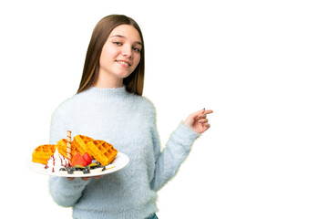 Teenager girl holding waffles over isolated chroma key background pointing finger to the side