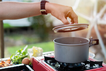 Shot of hand opening the Shabu-Shabu pot with set on picnic stove with vegetables