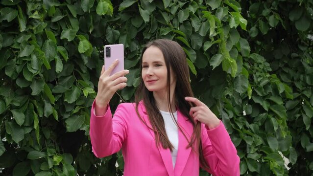 A woman takes a selfie using a smartphone camera on the street. A girl in a pink jacket smiles while taking a picture on the phone on the stree