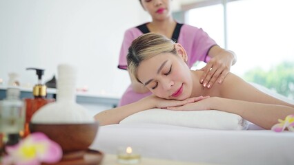 Obraz na płótnie Canvas Therapist massaging back of asian woman in totwel lying on bed relaxing during spa massage. Beautiful young asian woman lying on spa bed and relaxing while massaging back. Body relaxation concept