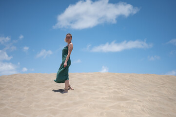 Fototapeta na wymiar Blond young girl with green dress in the breeze of the beach dunes
